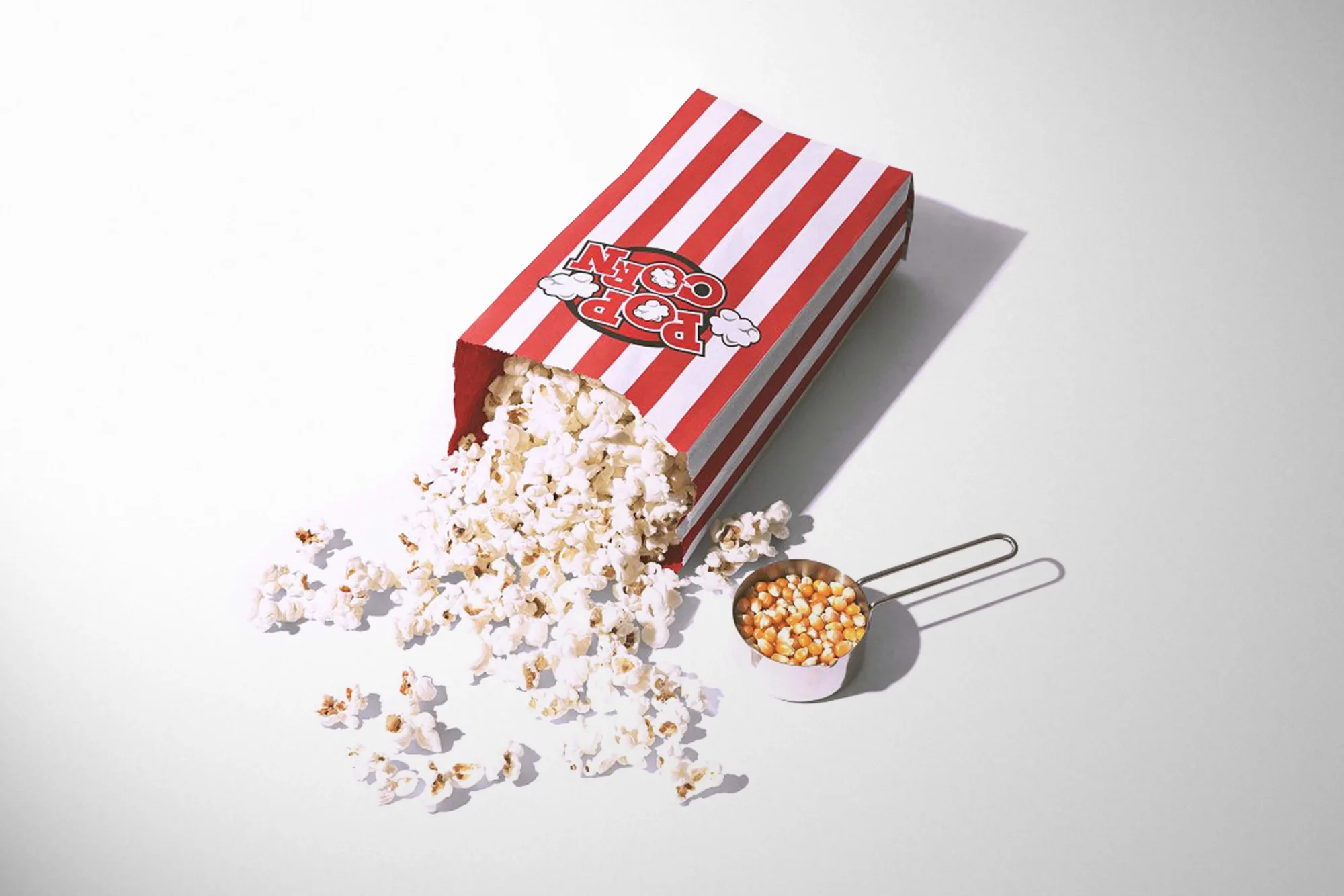 Popcorn spilling out of red and white striped box on white background, cinema snack concept